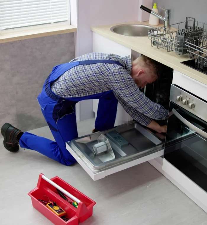 Technician servicing an open dishwasher beside a kitchen sink
