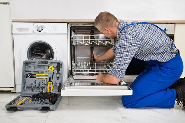 Technician checking the interior of an open dishwasher beside a washing machine
