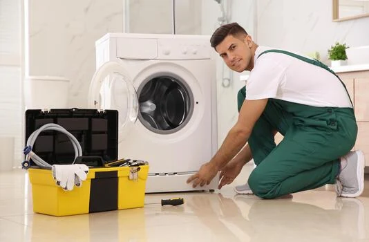 Technician inspecting a front-loading washing machine with a yellow toolbox nearby